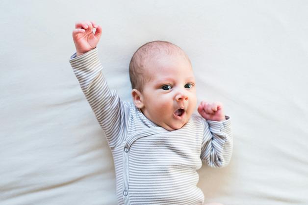 Bébé hyperactif souriant avec un bras levé, exprimant son énergie sur un fond neutre.