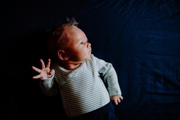 Bébé hyperactif en position couchée sur un lit, faisant des gestes avec ses mains.