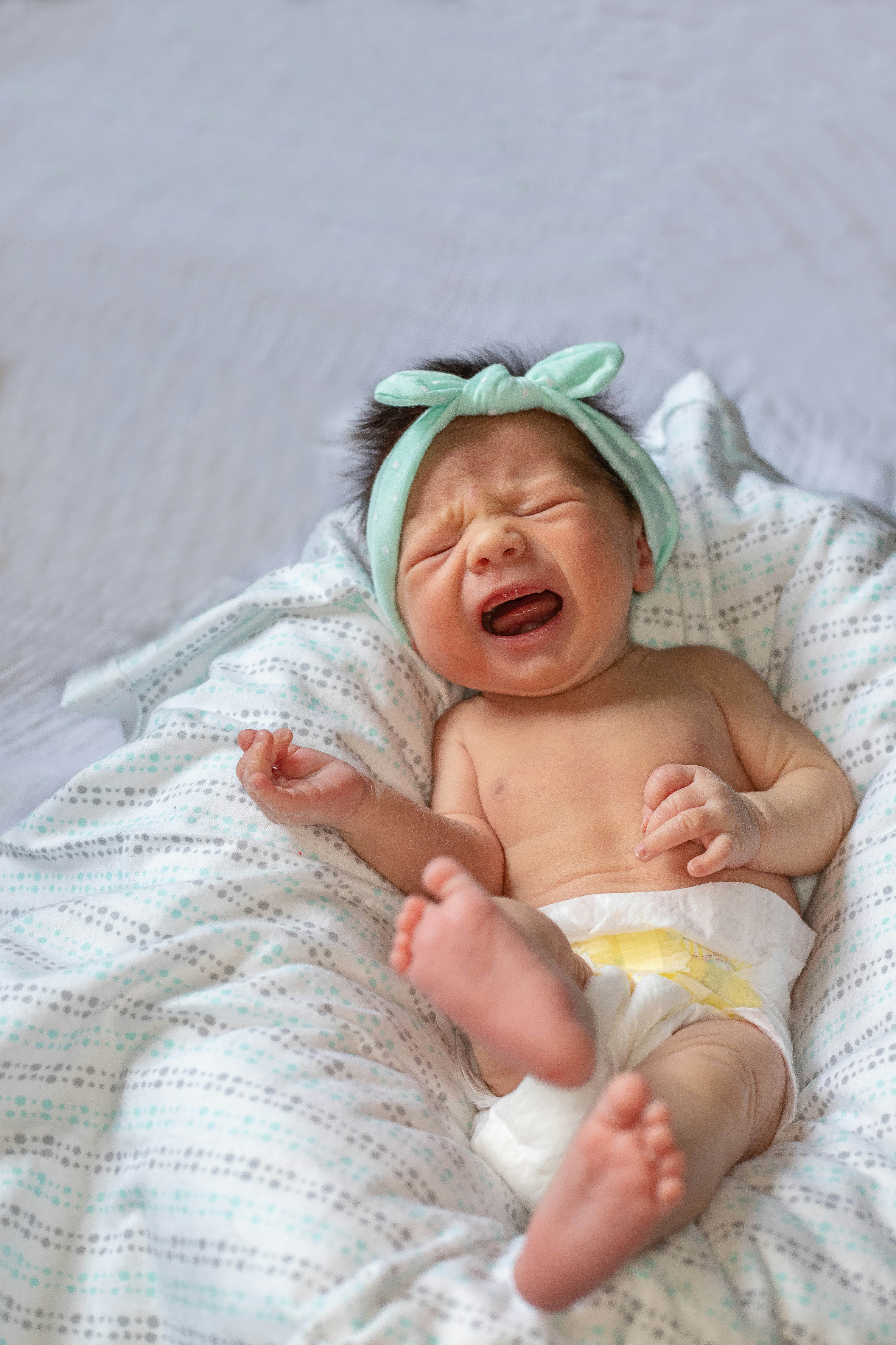 bébé malade qui pleure, allongé sur une couverture avec un bandeau, montrant des signes de détresse.