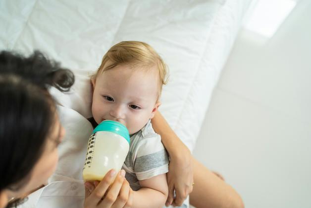 Un bébé tète un biberon contenant du lait maternel, illustrant l'importance de la conservation lait maternel.