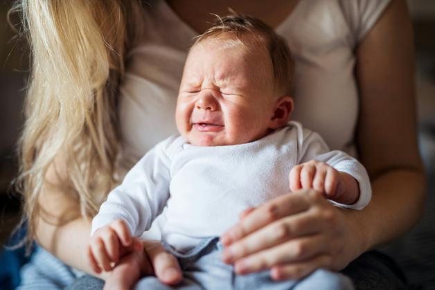 Bébé en pleurs sur les genoux d'un adulte, illustrant la problématique de la constipation des bébés.