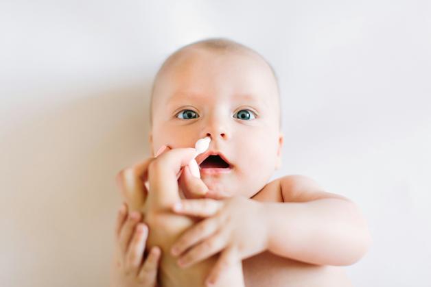 Bébé recevant un soin du visage avec une crème pour drp bébé sur un fond neutre.