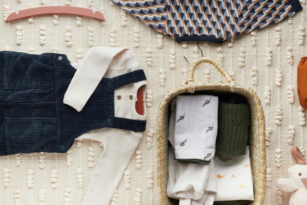 Image représentant des vêtements pour habiller bébé nuit avec un combiné en denim et des textiles doux dans un panier.