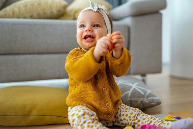 Un bébé souriant joue avec des jouets colorés, illustrant l'apprentissage de la langue des signes bébé.