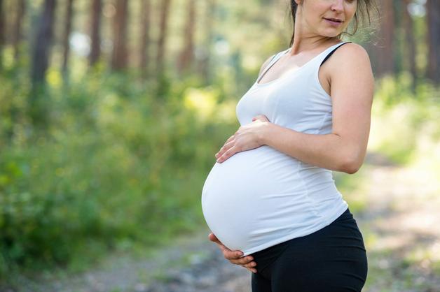 Femme enceinte touchant son ventre dans la nature, symbolisant le parcours de la MAP grossesse.