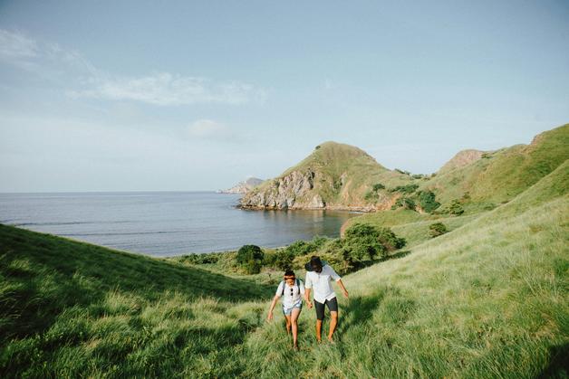 Couple marchant sur une colline verdoyante lors de leur babymoon grossesse, avec une vue sur la mer en arrière-plan.