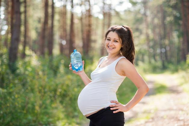 Femme enceinte dans la nature tenant une bouteille d'eau, évoquant l'importance la perte des eaux pendant la grossesse