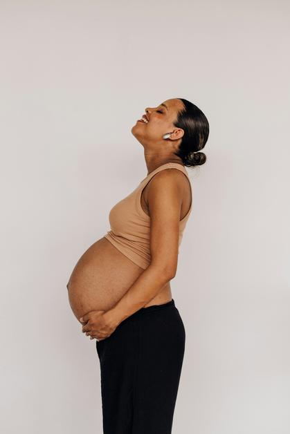 Femme enceinte souriante en profil, tenant son ventre, évoquant la thématique de la constipation enceinte.