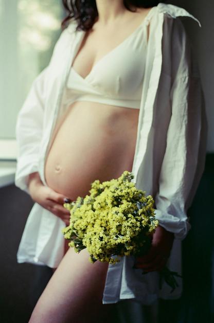 Femme enceinte tenant un bouquet de fleurs, illustrant les courbatures enceinte courantes pendant la grossesse.