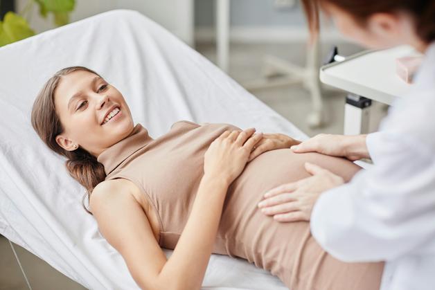 Femme enceinte souriante en consultation, évoquant ses douleurs aux côtes enceinte avec le médecin.