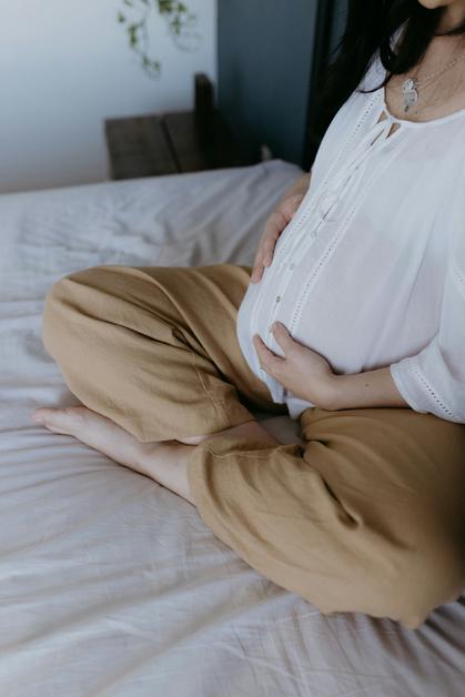 Femme enceinte assise sur un lit, tenant son ventre, illustrant les douleurs pelviennes enceinte.