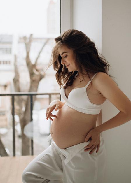 Femme enceinte en sous-vêtements blancs caressant tendrement son ventre, en attente de son accouchement