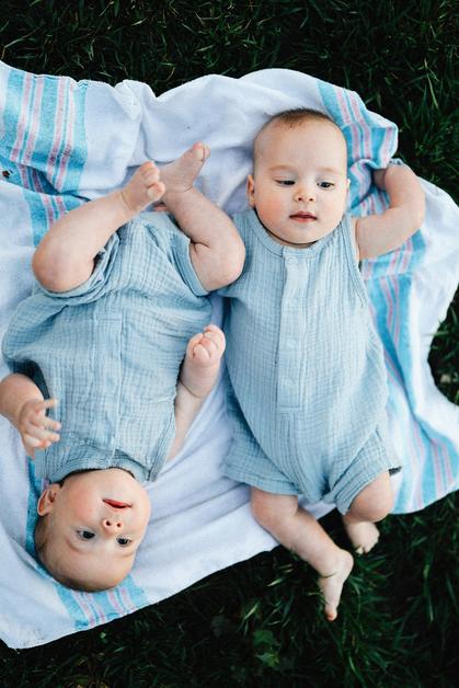 Image de jumeaux allongés sur une couverture, mettant en évidence leurs gros ventre jumeaux, souriant et jouant dans l'herbe.