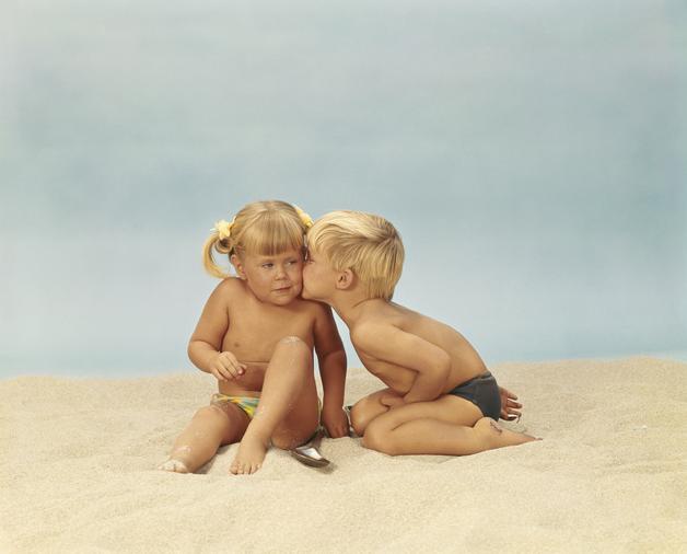 Jumeaux fille garçon jouant sur la plage, la petite fille assise et le garçon lui chuchotant à l'oreille.