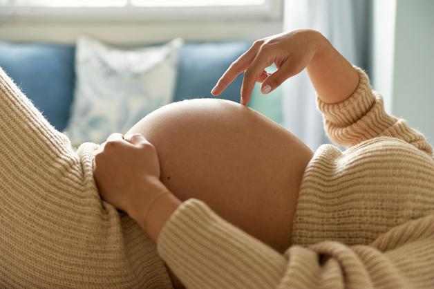 Femme enceinte allongée, touchant son ventre dans une position relaxante, illustrant les positions ouvrir col.