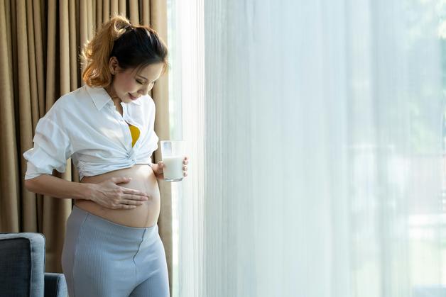 Femme enceinte tenant un verre de lait, réfléchissant sur les remontées acides enceinte.