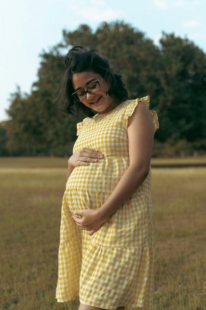 Femme enceinte souriante portant une robe à carreaux, évoquant l'importance de surveiller la rubéole grossesse.