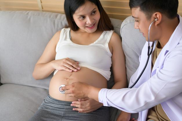 Consultation médicale sur le streptocoque B grossesse, avec un médecin écoutant le ventre d'une patiente enceinte.