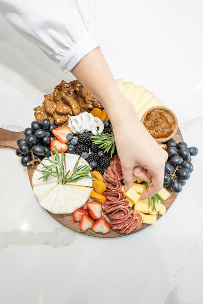 Une main prenant un morceau de fromage sur un plateau de charcuterie, où l'urine orange grossesse peut être un signe à surveiller.