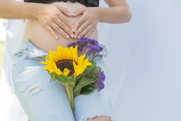 Femme enceinte caressant son ventre, symbolisant les varices vulvaires grossesse avec des fleurs.