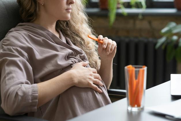 Femme enceinte réfléchissant aux aliments interdits enceinte, avec des carottes à portée de main.