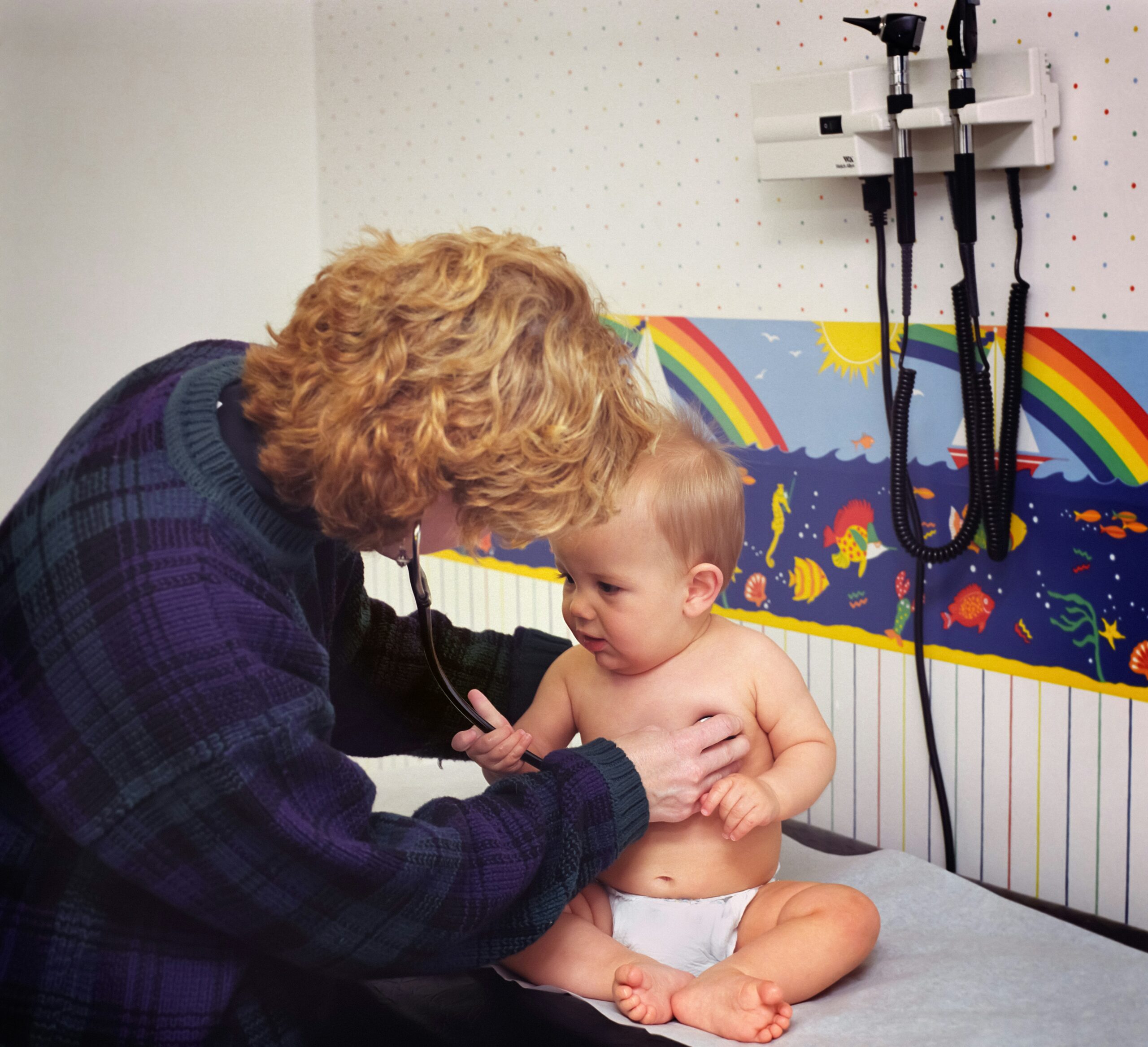 Bébé en consultation avec un pédiatre qui l’ausculte avec un stéthoscope dans un cabinet médical coloré