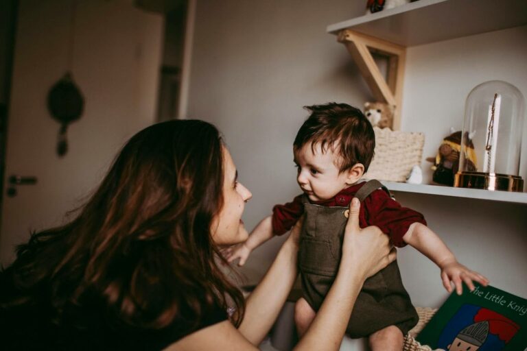 Femme tenant un bébé dans ses bras dans une chambre décorée de jouets et livres pour enfants.