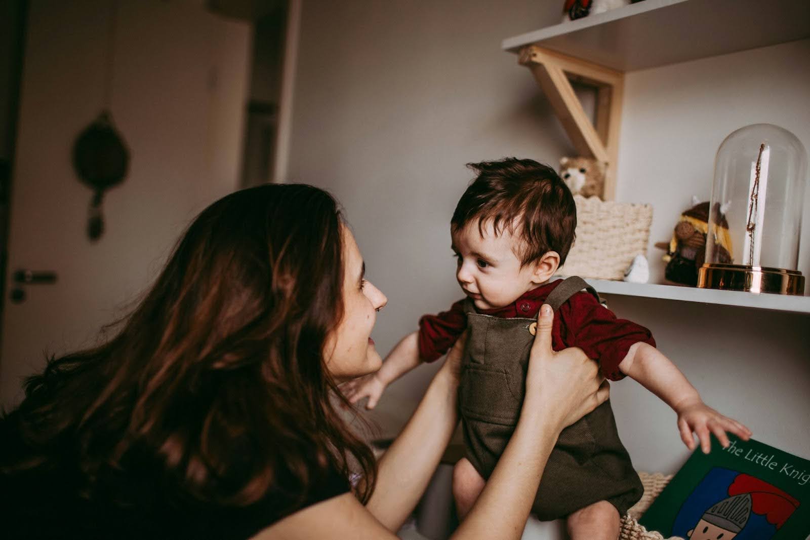 Femme tenant un bébé dans ses bras dans une chambre décorée de jouets et livres pour enfants.