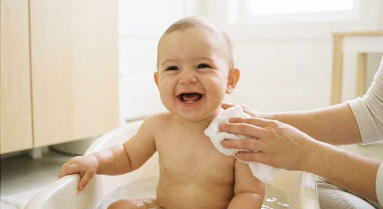 Smiling baby being washed with a washcloth illustrating the dilemma of what to wash baby with washcloth or sponge